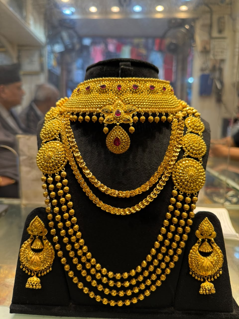 Gold bridal set on a black display: a choker set with red stones, several gold strands, and a pair of gold earrings