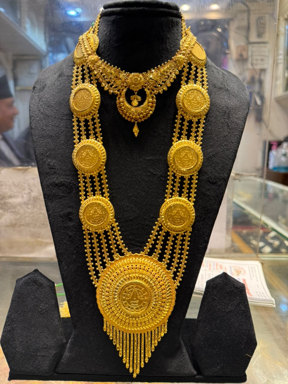 Multi-strand gold necklace with coin-like medallions, a large round pendant and a gold fringe, worn with a shorter necklace