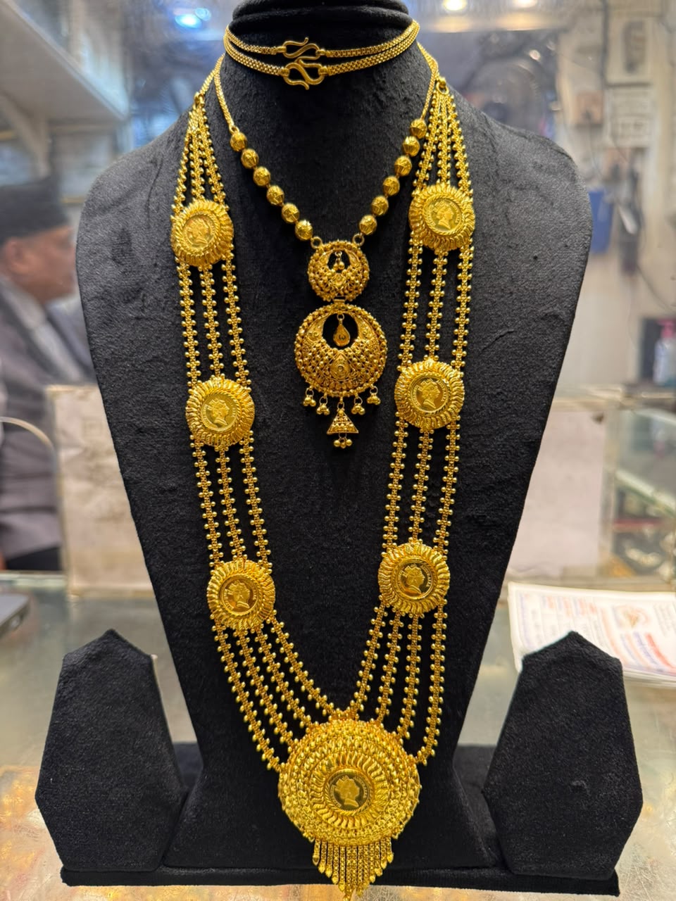 Gold necklace of several strands with round coin-like medallions, worn with a shorter gold necklace
