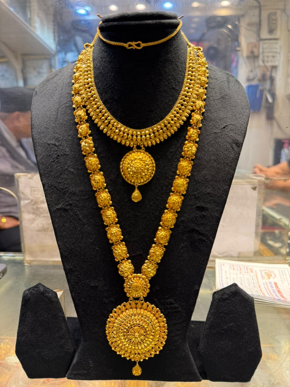Layered gold necklace: a short collar with a round pendant, and a longer chain of floral links with a large round pendant