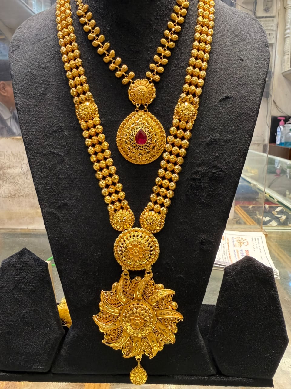 Gold necklace with a red-stone teardrop pendant and a larger lotus-shaped pendant
