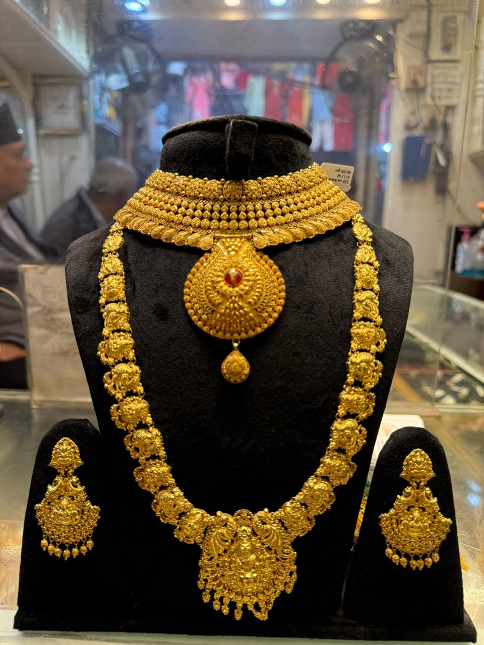 Gold choker and longer necklace with matching earrings; a red stone sits in the upper pendant